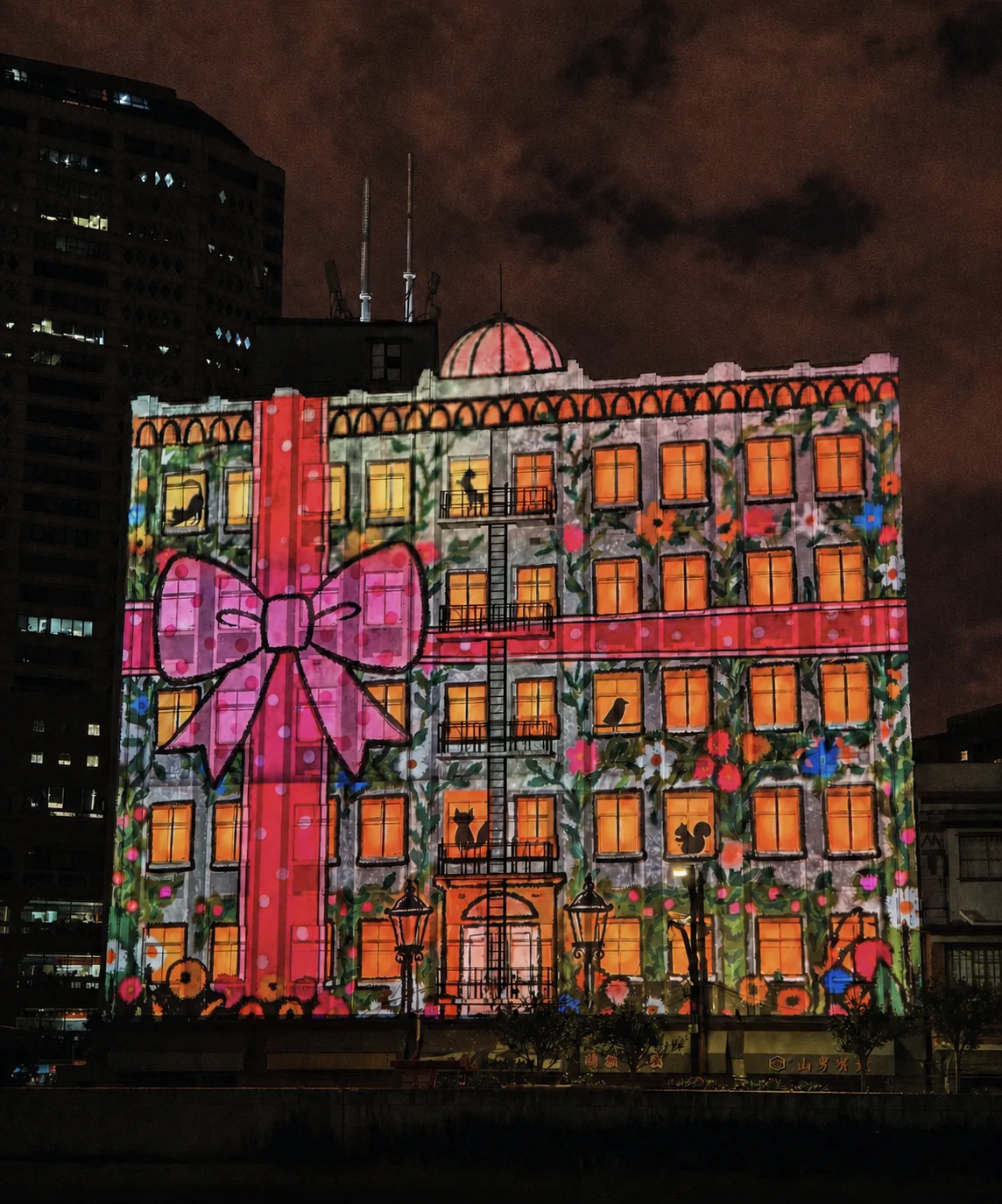 AI-created editorial visual of a historic façade illuminated with a large pink ribbon and floral projection at night, inspired by 2025 festival highlights