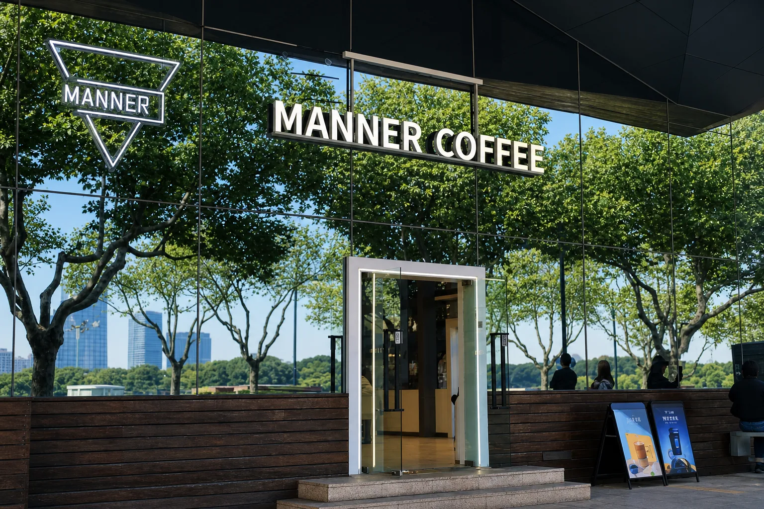 Une devanture réfléchissante de MANNER COFFEE où se reflètent des arbres verts en été