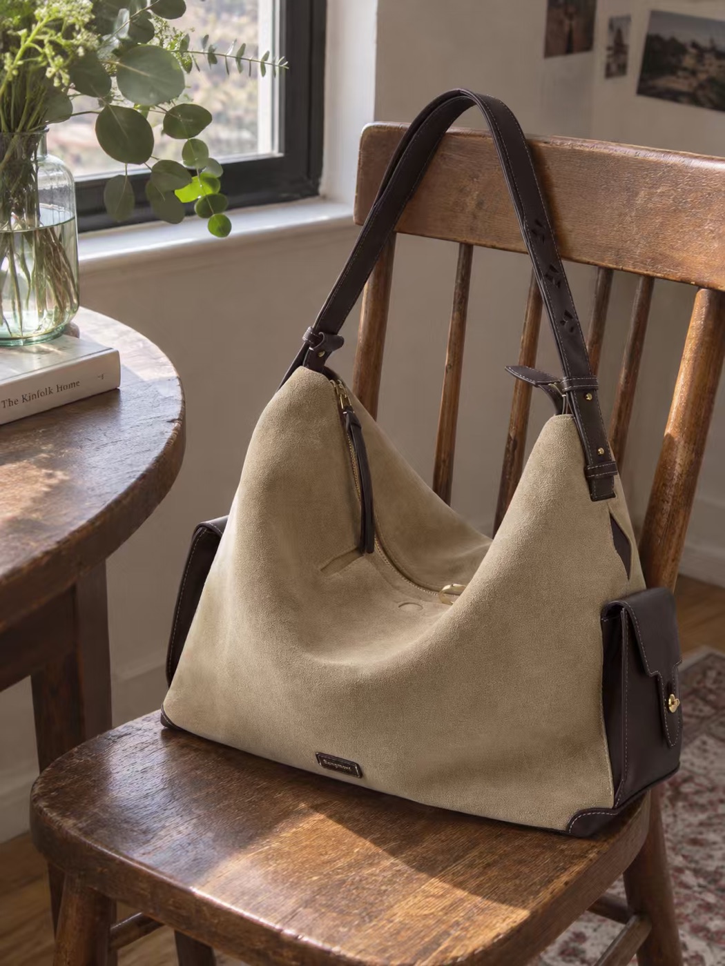 A beige Songmont bag with dark straps on a wooden chair